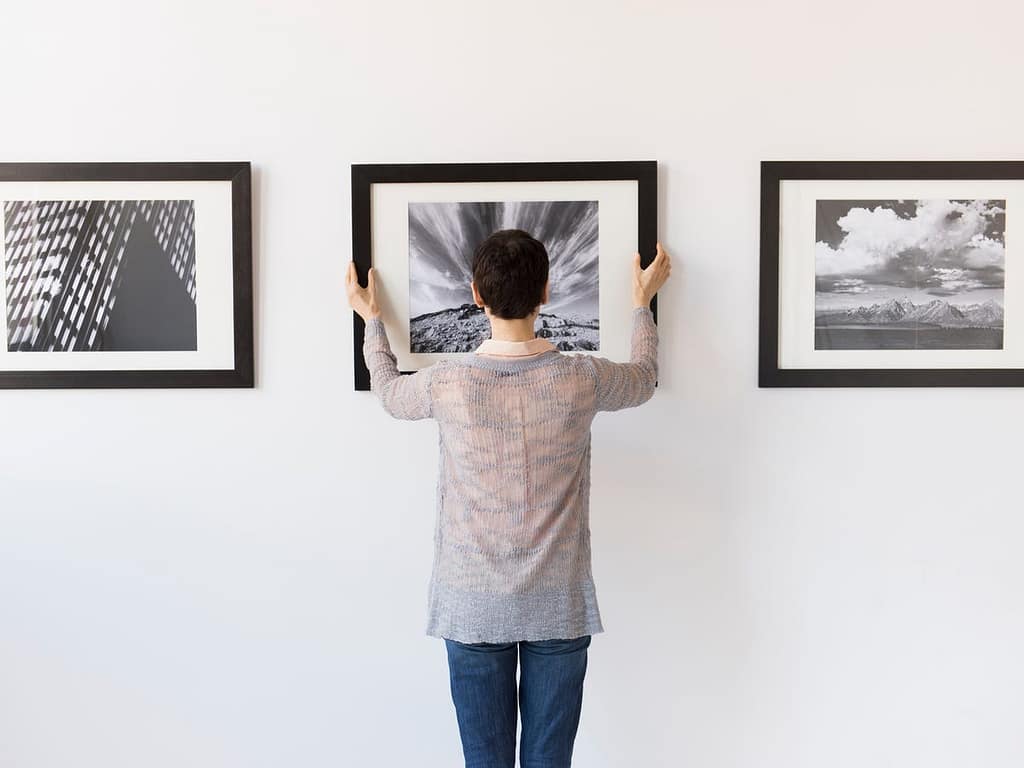Professional artwork installation technician in Dubai hanging a wall frame on a concrete wall.