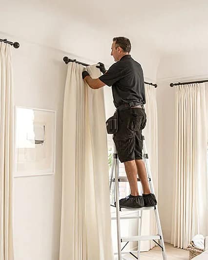 Professional curtains installer in Dubai fitting a curtain rod on a concrete wall.