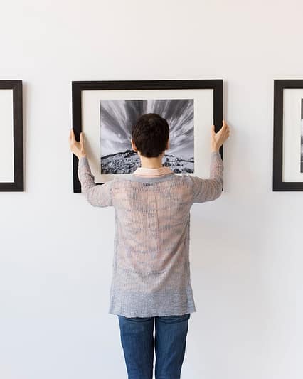 Professional artwork installation technician in Dubai hanging a wall frame on a concrete wall.