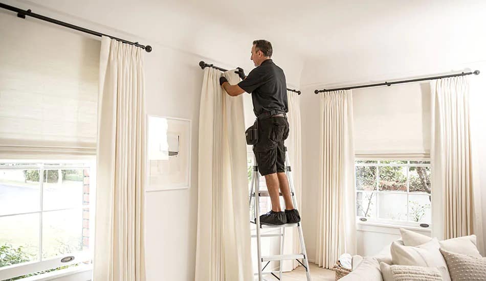 Professional curtains installer in Dubai fitting a curtain rod on a concrete wall.